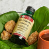 Bottle of Adathodai Manappagu surrounded by its raw ingredients and a cup containing the medicine